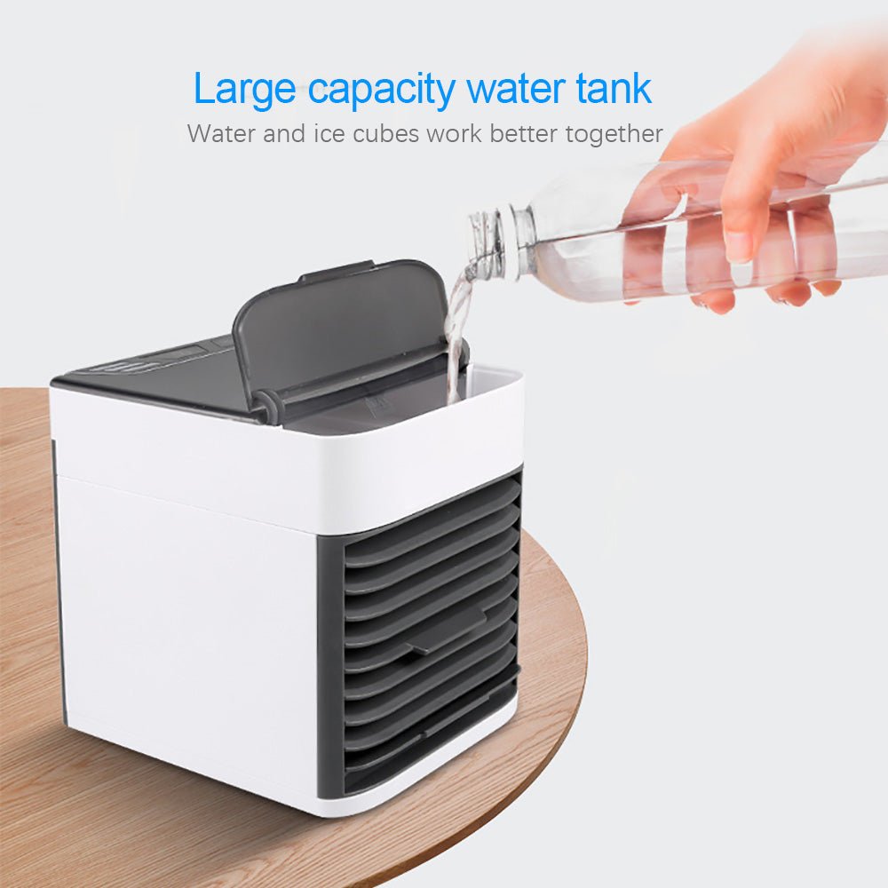 Small air cooler fan with a large capacity water tank on a wooden surface, showing a hand pouring water from a bottle.